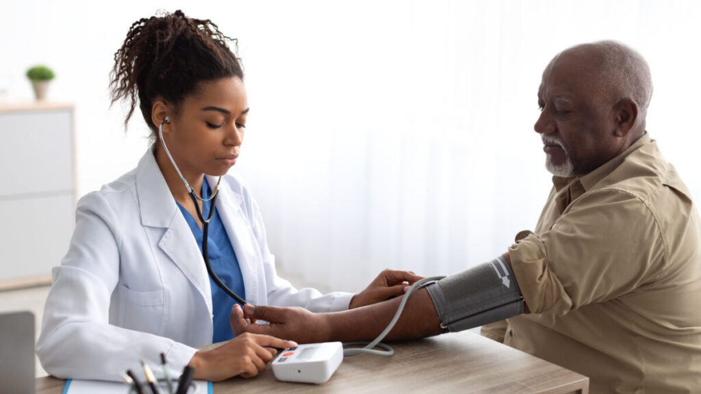 A female doctor is checking the blood pressure of an older black man