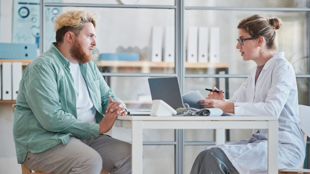 Overweight man sitting at the table together with doctor and talking about his health during his visit.