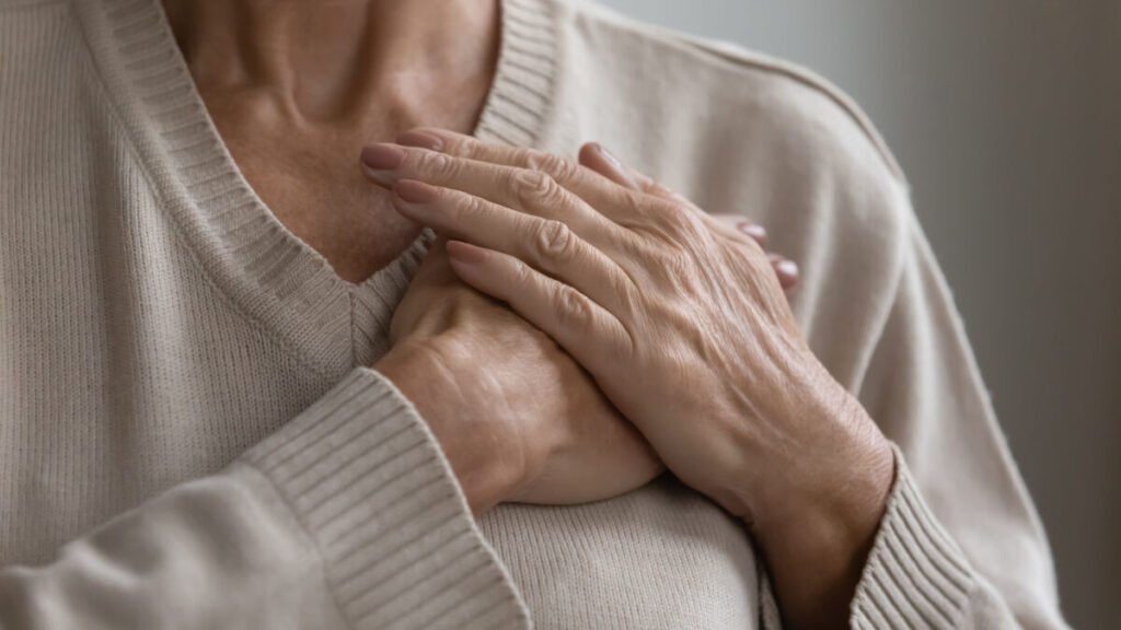Elderly female holding her hands against her chest, appearing as though she is experiencing pain from her heart.